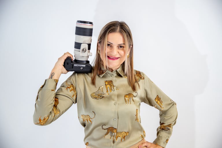 Woman in khaki wildlife-patterned shirt holding professional telephoto lens camera over her shoulder against white background