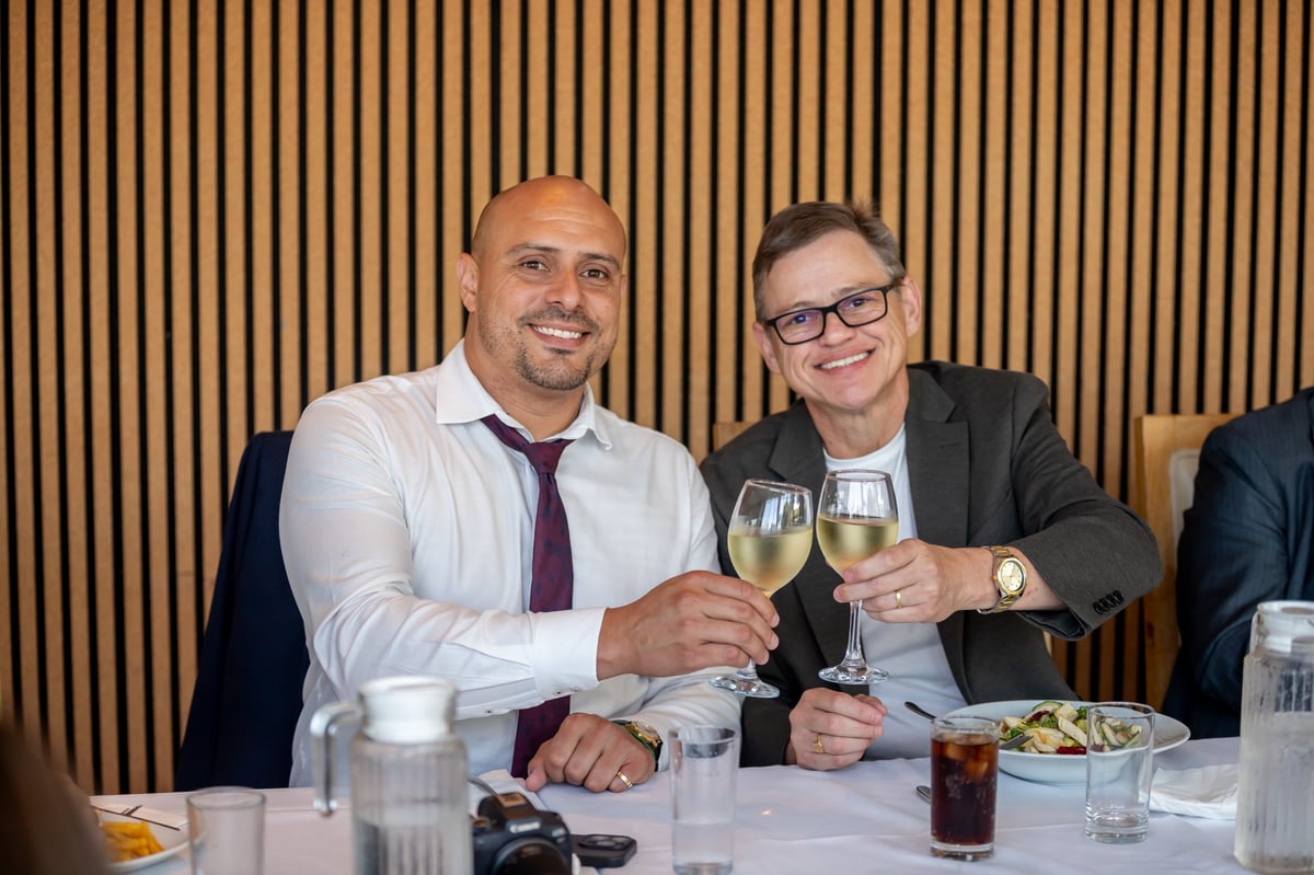 Two men in business attire toasting with white wine glasses at a formal dining table.