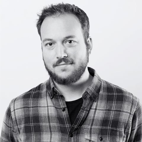 Black and white portrait of a man with a full beard wearing a plaid shirt against a light background