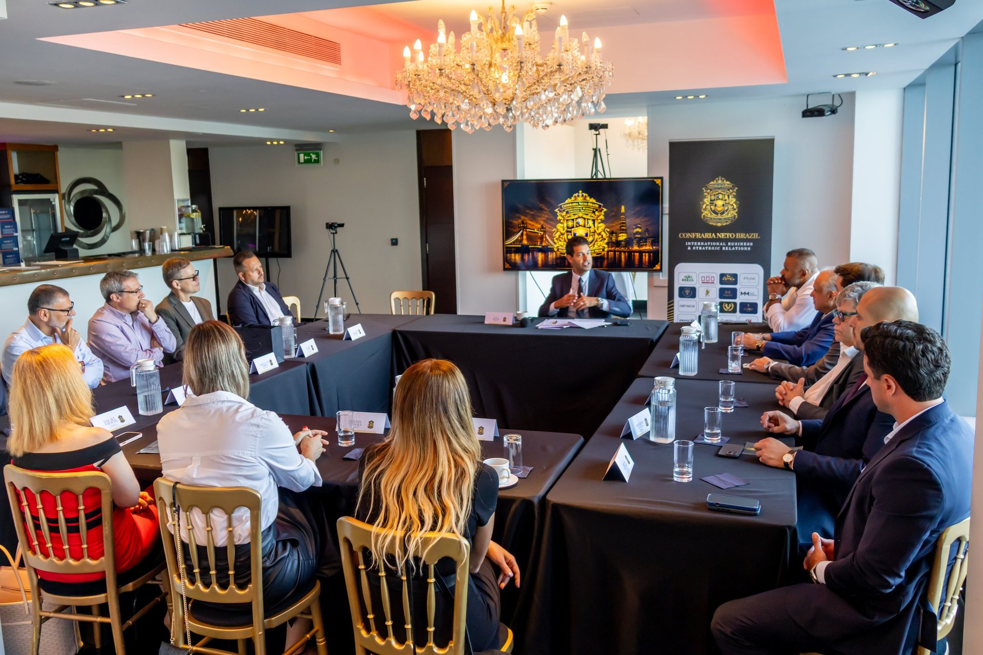 Business meeting in modern conference room with attendees seated around black table under ornate chandelier
