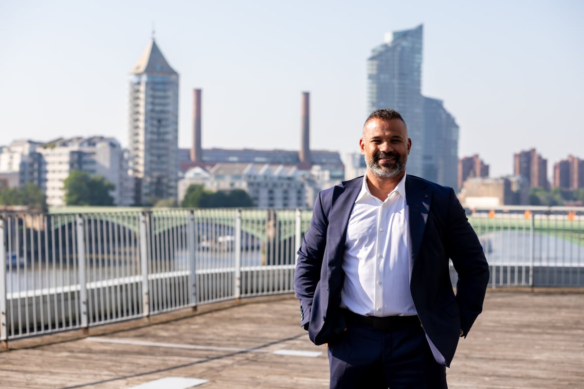 Man in business suit standing on waterfront deck with city skyline in background