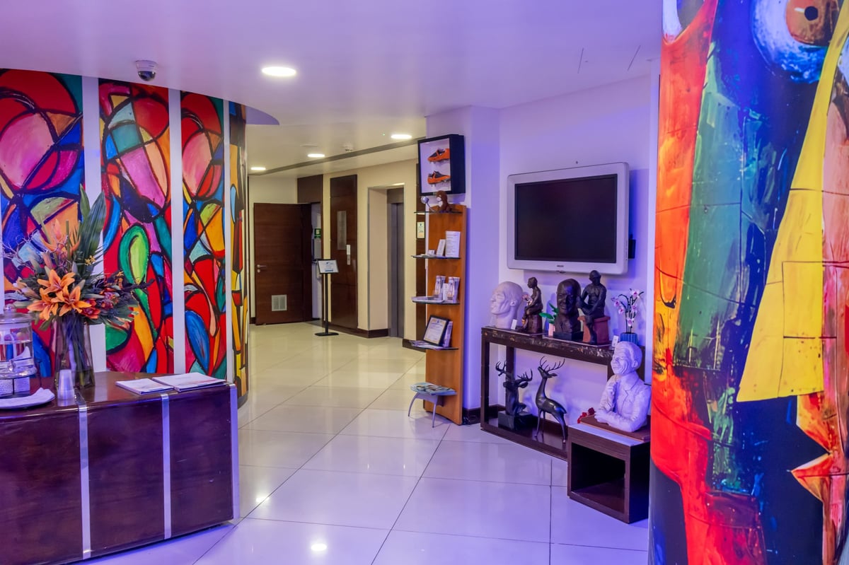 Modern living room interior with vibrant neon artwork on walls, purple ambient lighting, TV, and colorful abstract paintings