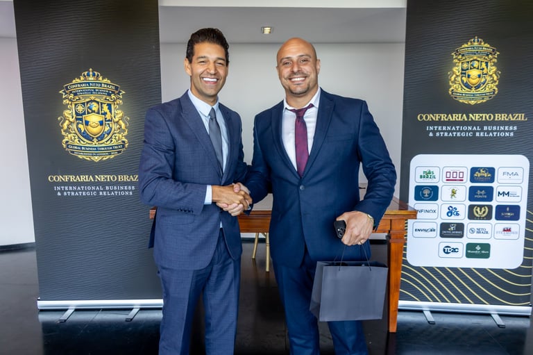 Two men in business suits shaking hands in front of Consfraria Neto Brazil branded banners and logos