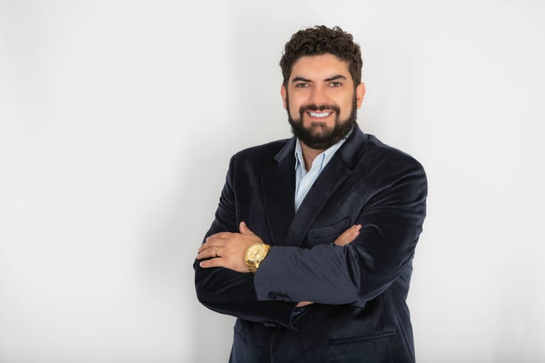 Bearded man in navy blazer with arms crossed smiling at camera against white background