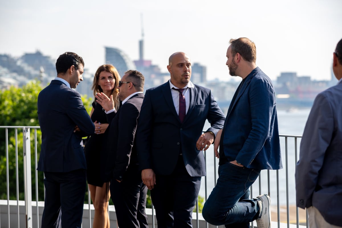 Business professionals in suits conversing on an outdoor rooftop terrace with a city skyline in the background