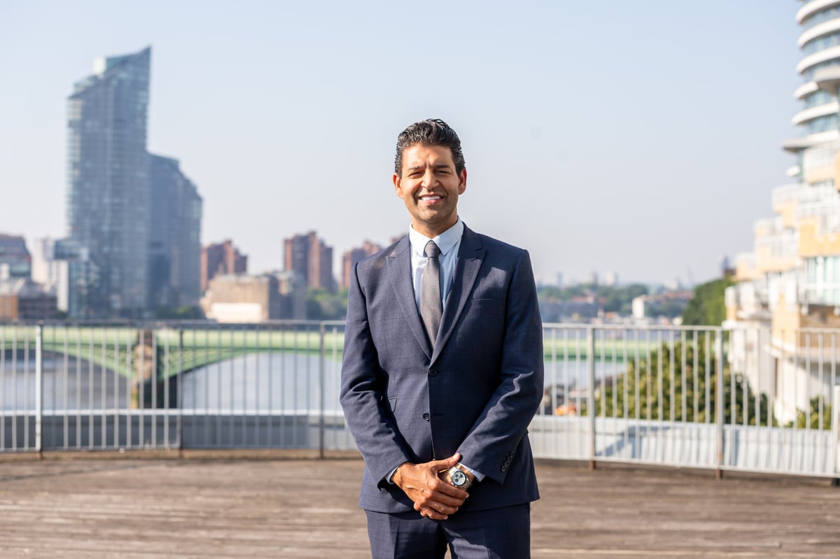 Professional man in dark business suit smiling on rooftop terrace with city skyline and river in background
