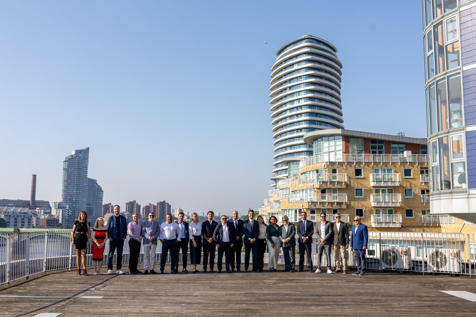 Group of business professionals standing on a rooftop deck with modern city buildings and blue sky in background