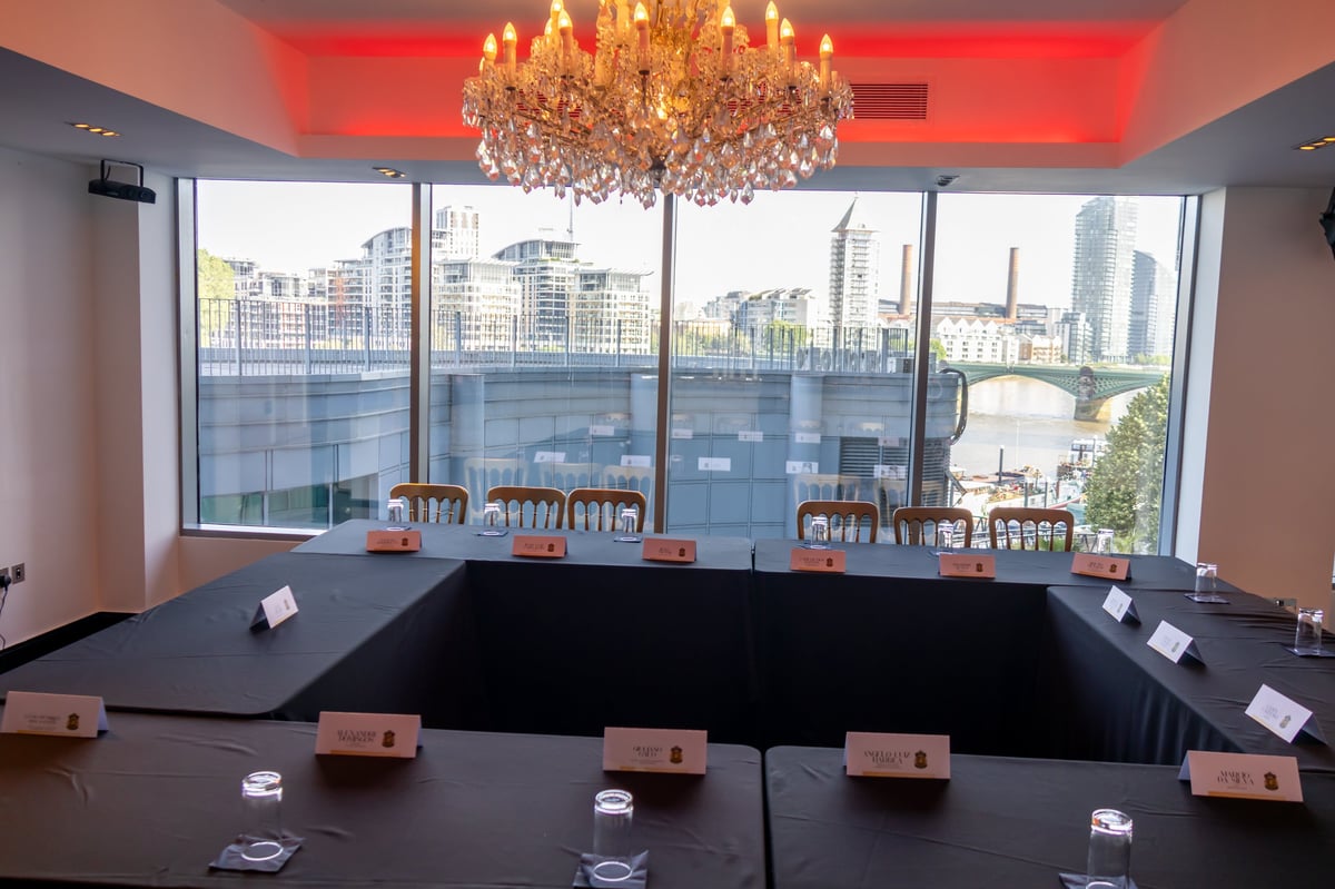 Modern conference room with crystal chandelier, red accent ceiling, and floor-to-ceiling city skyline views through glass windows.