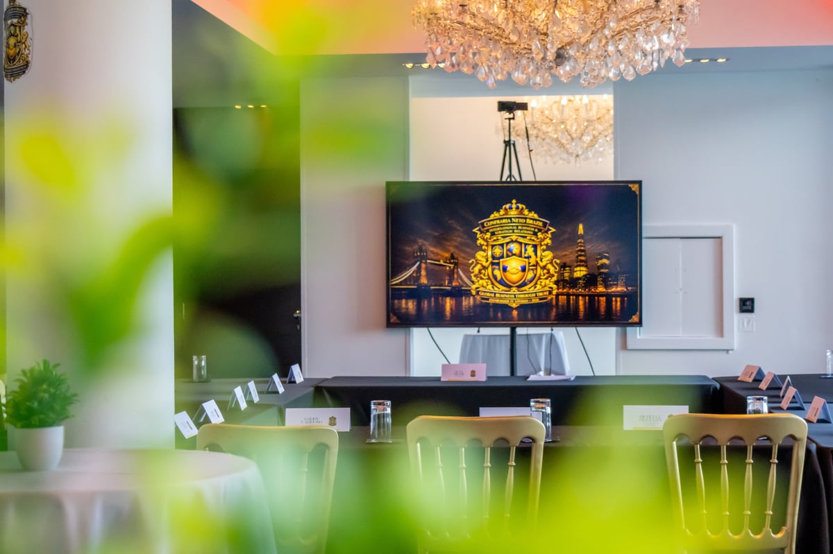 Modern conference room with flat-screen TV displaying illuminated temple, wooden chairs, pendant lighting, and green plant foliage in foreground