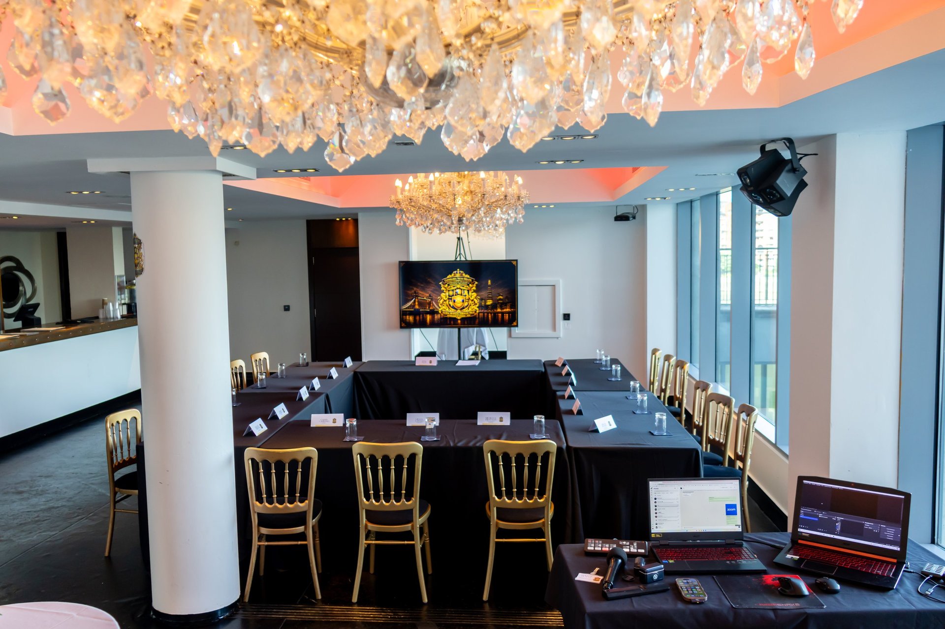 Elegant conference room with black table, gold chairs, crystal chandelier, and modern two-tone ceiling with orange and blue tones.