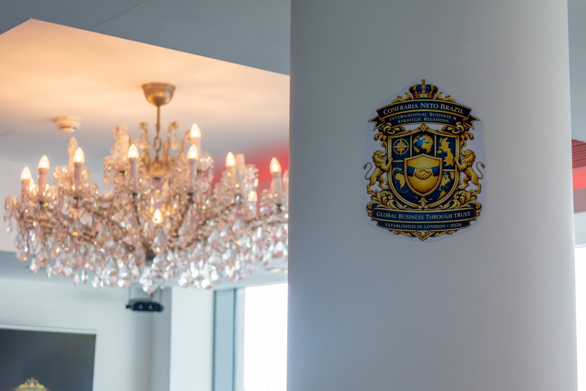 Ornate crystal chandelier hanging from ceiling with gold decorative crest mounted on white wall