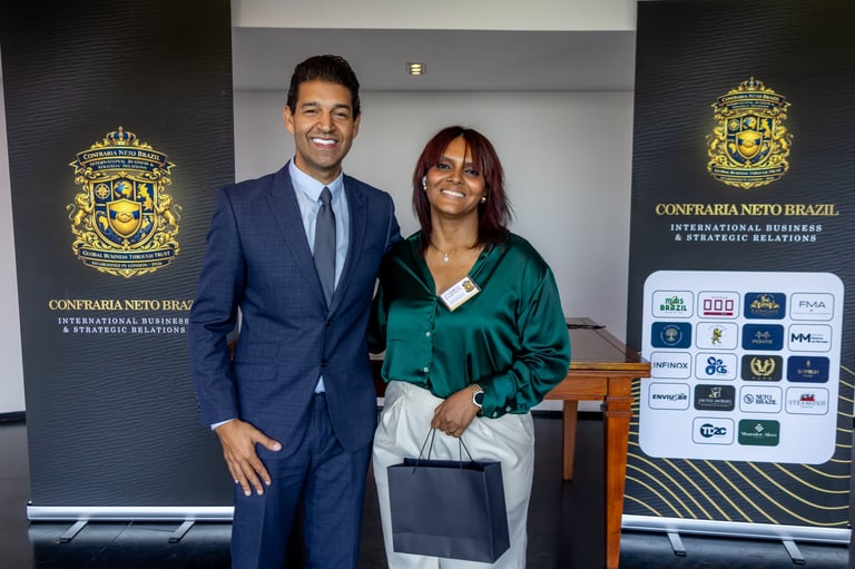 Man in blue suit and woman in green jacket posing together at a formal event with logos visible in background
