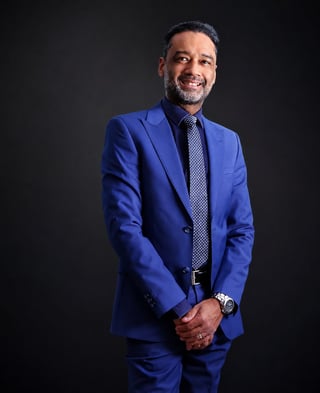 Professional man in a blue suit and patterned tie smiling at the camera against a dark background
