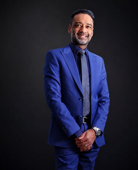 Professional man in a blue suit and patterned tie smiling at the camera against a dark background