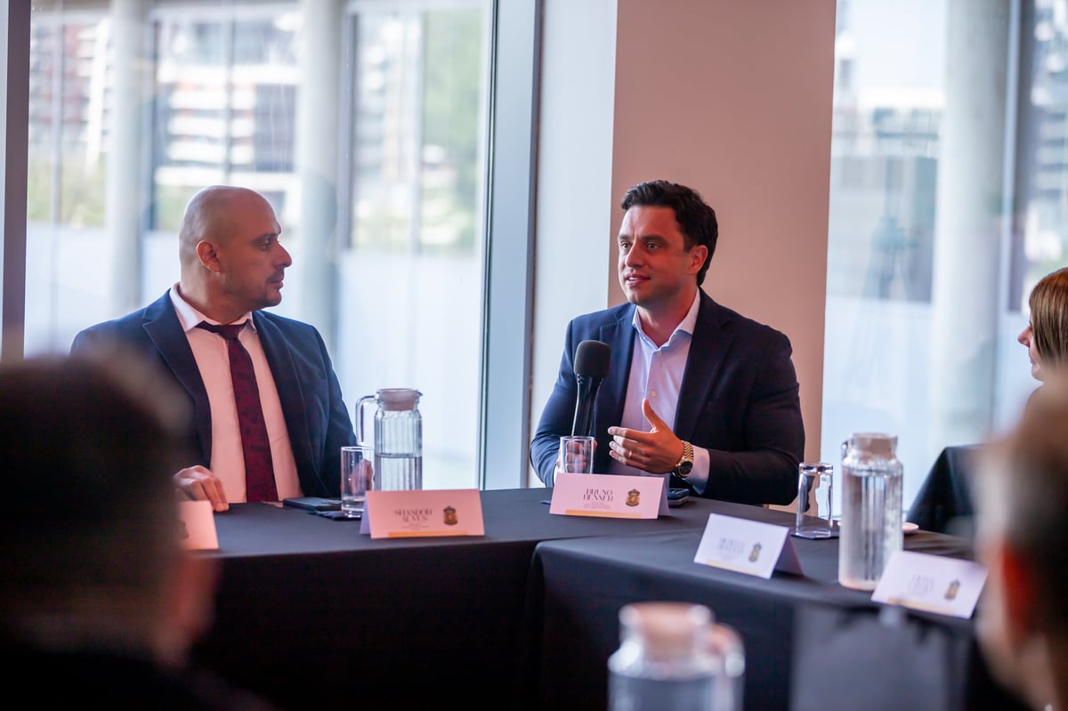 Two businessmen in suits sit at a conference table with water glasses, discussing during a corporate meeting in a high-rise office