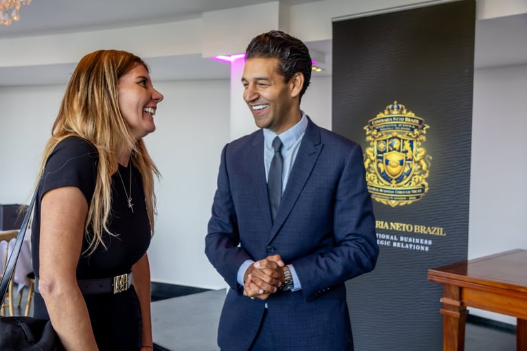 Man in navy suit and woman in black shirt shake hands and smile inside an office with Brazilian embassy signage