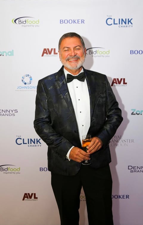 Man in black tuxedo with patterned jacket and bow tie posing at event with branded backdrop