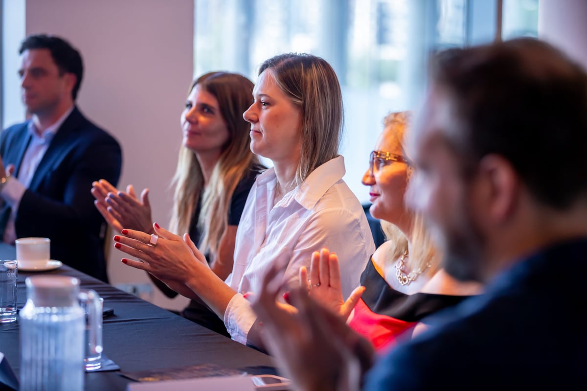 Professionals sitting at a table in a modern office, clapping and celebrating during a business meeting or presentation event