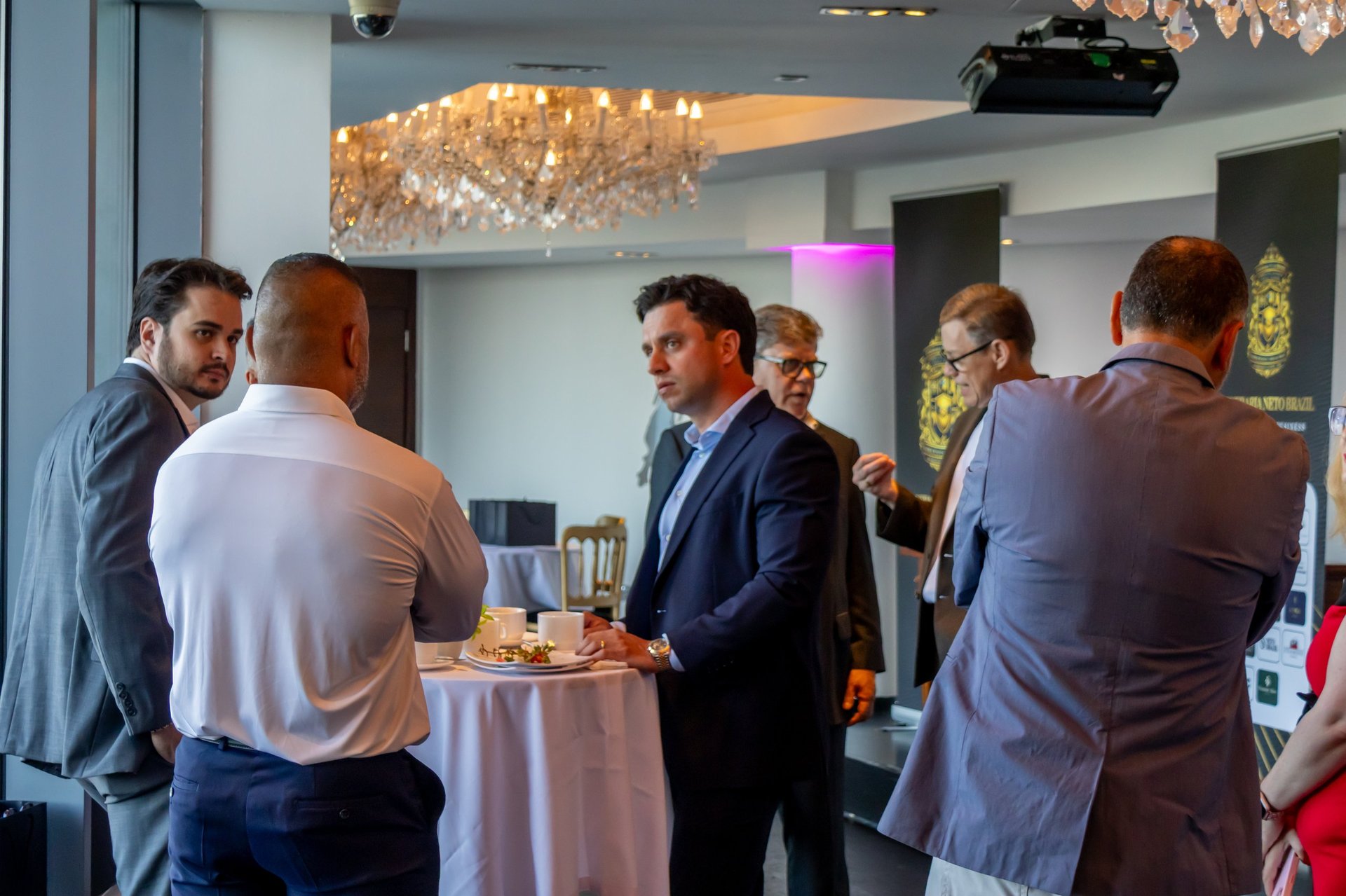 Group of men in business casual attire networking at an indoor event with elegant golden chandelier lighting and modern decor