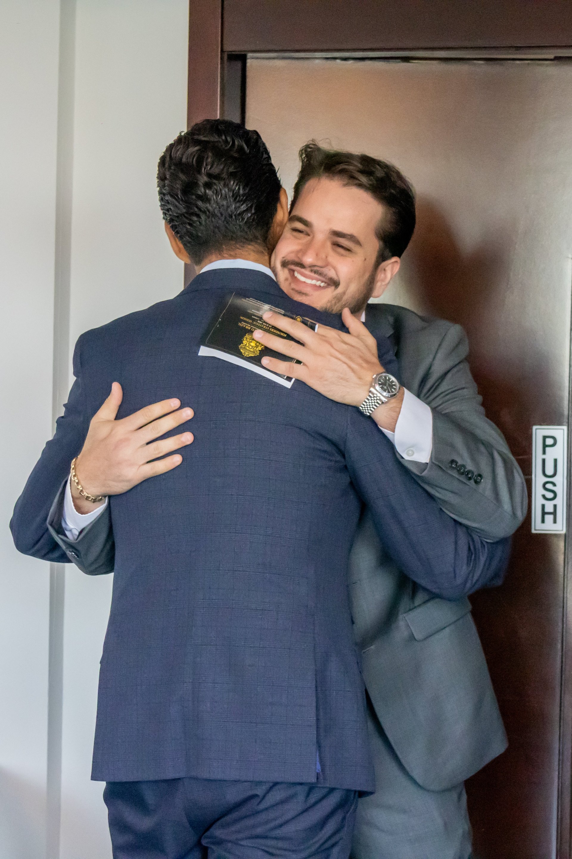 Two men in business suits embracing and smiling warmly near a doorway, appearing happy and friendly