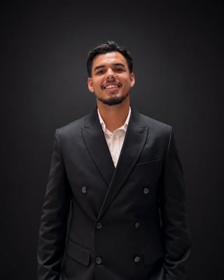 Man in black double-breasted blazer with white shirt smiling against dark background