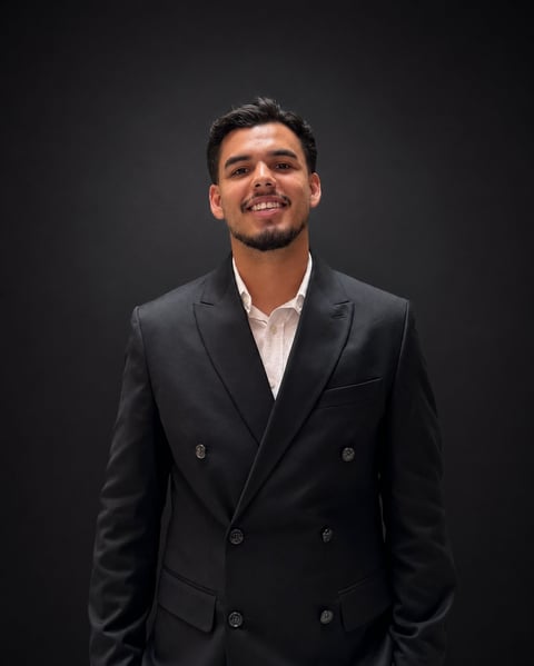 Man in black double-breasted blazer with white shirt smiling against dark background