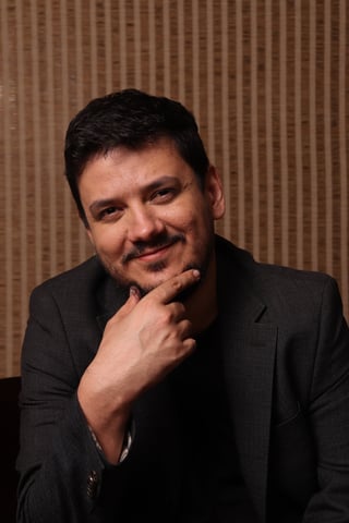 Man in dark blazer with hand to chin in thoughtful pose against textured brown background