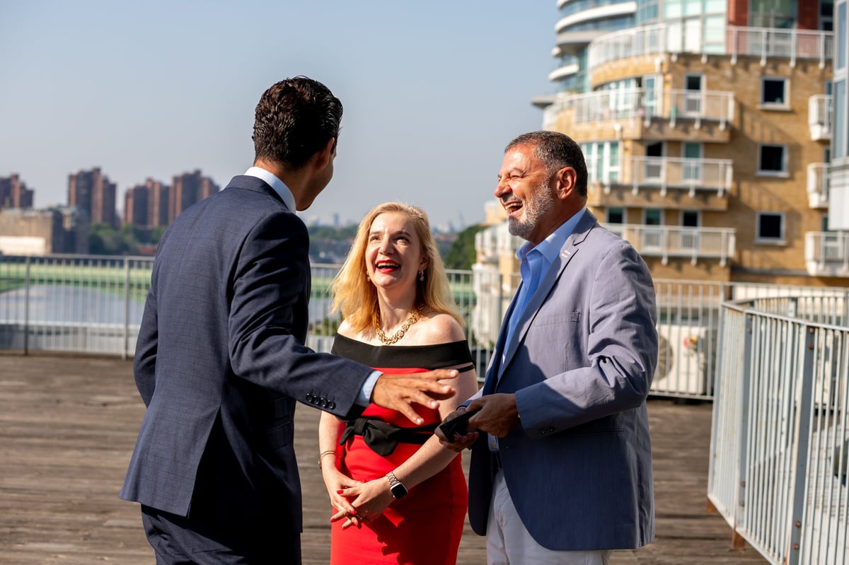 Three business professionals in suits shaking hands on a rooftop with city skyline in the background