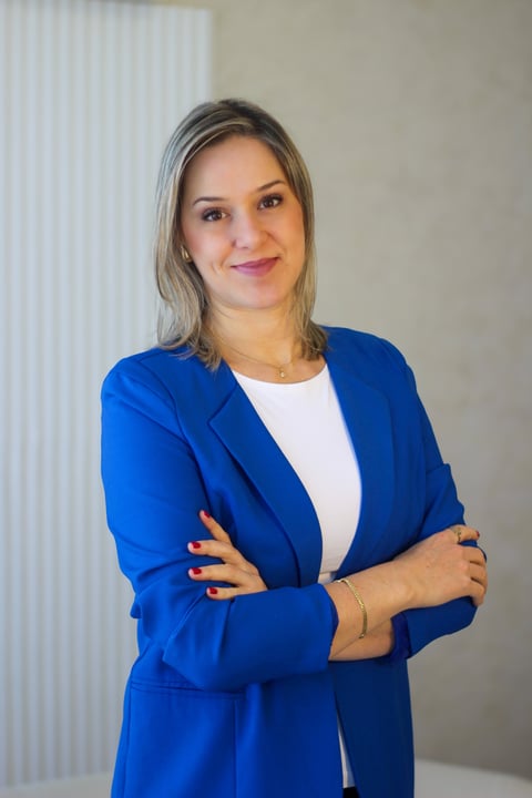 Professional woman wearing a blue blazer and white top, arms crossed, smiling at camera against neutral background