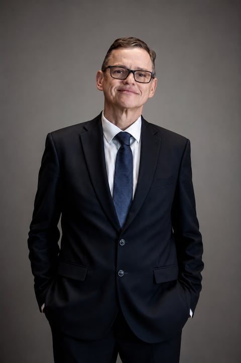Professional man in business suit with glasses and blue tie smiling against gray background