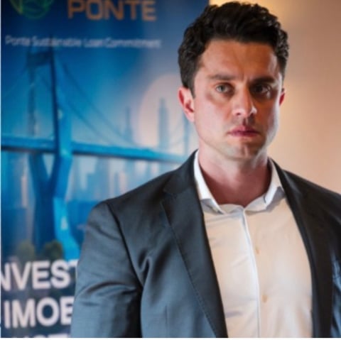 Professional man in dark blazer and white shirt standing in front of blue bridge backdrop