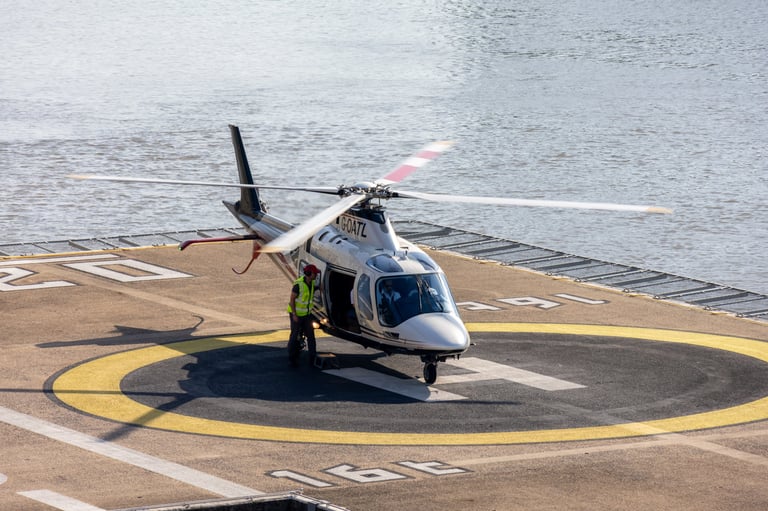 White and blue helicopter parked on a yellow and black circular helipad with water visible in the background