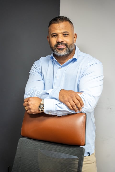Professional man in light blue shirt holding brown leather clutch, standing against two-tone gray and white background